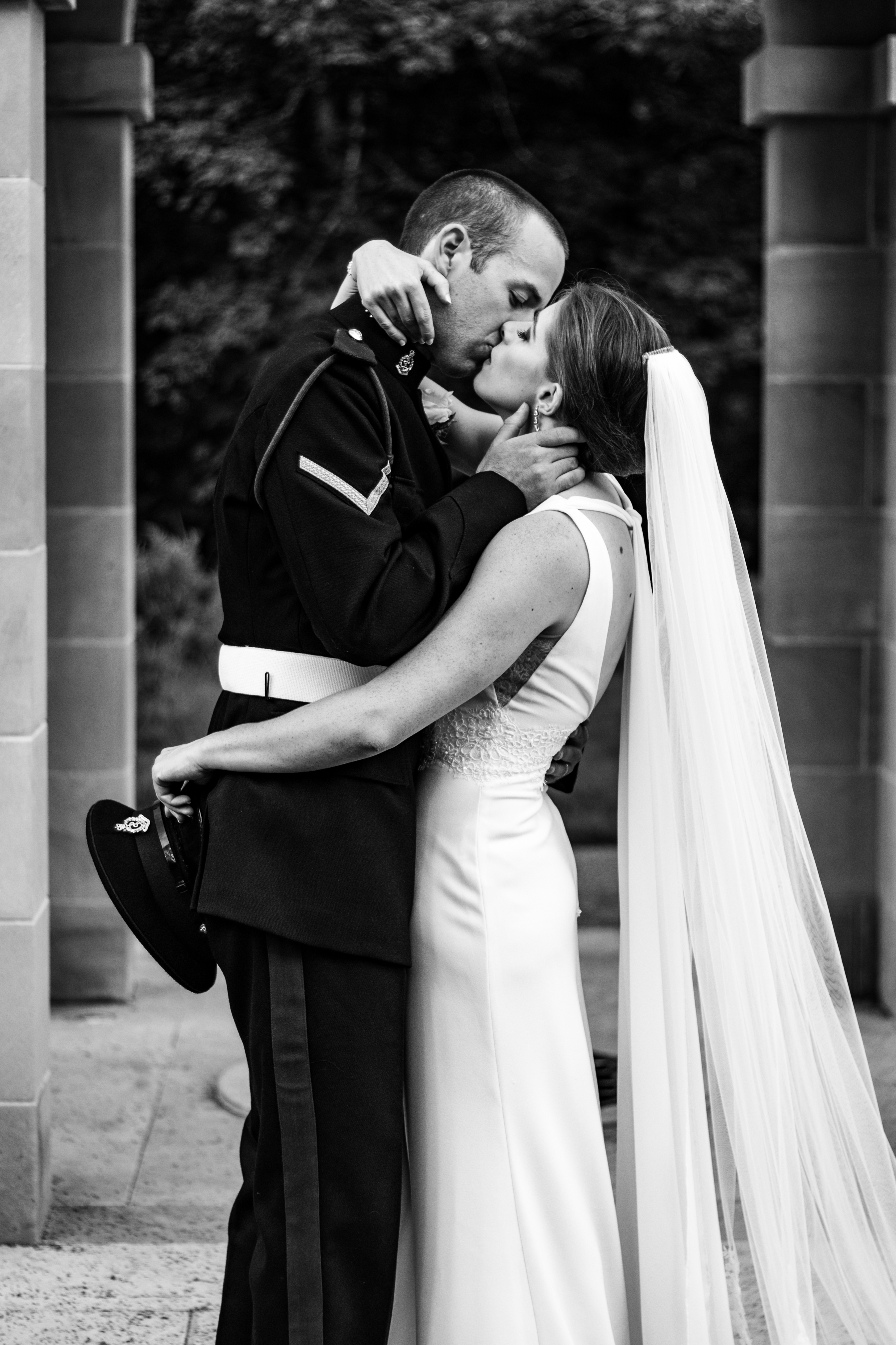 Anna & David — black and white kiss between military groom and bride beneath stone pillars